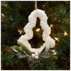 an ornament hanging from a christmas tree decorated with white yarn and greenery