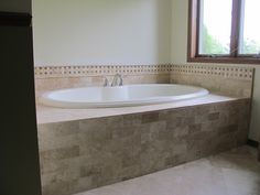 a bath tub sitting next to a window on top of a tiled floored bathroom