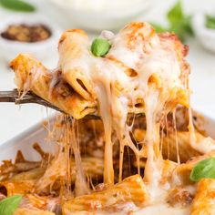 a slice of pizza being lifted from a casserole dish with cheese and basil