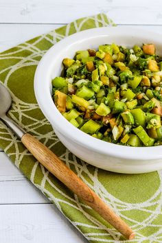 a white bowl filled with chopped vegetables on top of a green napkin next to a wooden spoon