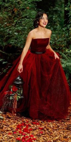 a woman in a red dress is posing for a photo with leaves on the ground