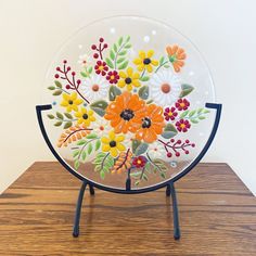 a glass plate with flowers painted on it sitting on a wooden table next to a white wall