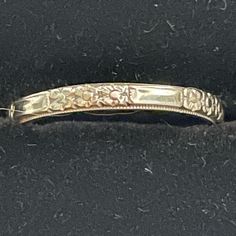 an antique yellow gold wedding band with flowers and scrolls on the side, set against a black background