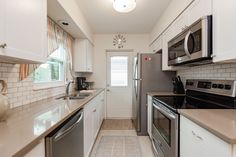 a kitchen with stainless steel appliances and white cabinets, along with beige tile flooring