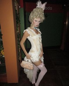 a woman dressed up in a costume and holding a purse standing next to a wall