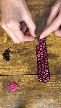 two hands are making beaded bracelets with pink beads on a wooden table top