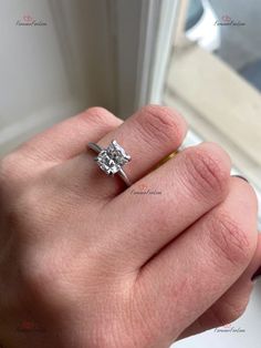 a woman's hand with a diamond ring on top of her finger, in front of a window