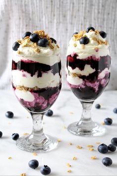 two desserts with blueberries and yogurt in them on a white table