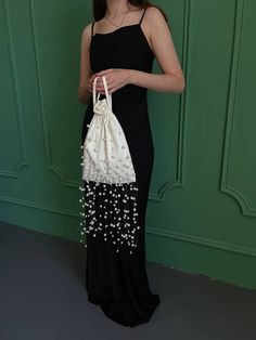 a woman in a black dress is holding a white bag with pearls on the bottom