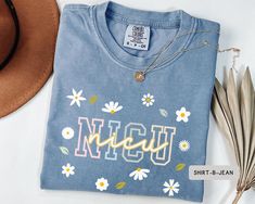 Stay comfortable and stylish with our Daisy NICU Nurse Comfort Colors® T-Shirt. This floral tee is perfect for mother-baby nurses and NICU crew staff, offering a soft, vintage-inspired look. A thoughtful gift for dedicated healthcare professionals! PRODUCT DETAILS *High Quality Comfort Colors® T-Shirt 1717 *Made with medium fabric (6.1 oz/yd² (206.8 g/m²) *100% ring-spun US cotton for long-lasting comfort. *Preshrunk, soft-washed, garment-dyed fabric brings extra coziness to your wardrobe while Blue Tops With Name Print For Spring, Mother Baby Nurse, Baby Nurse, Nurse Shirts, Nursing Baby, Nicu Nurse, Mother Baby, Floral Tee, Mother And Baby