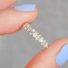 a woman's hand holding an engagement ring with five stones on it and blue nail polish