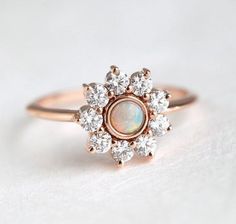 an opal and diamond cluster ring on a white surface, with the center stone surrounded by smaller round diamonds