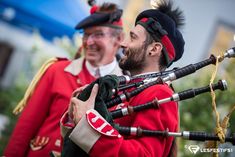 two men in red uniforms are playing bagpipes and singing into each other's ears