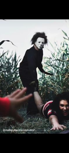 two people are in the grass and one person is wearing a mask while another person holds out their hand