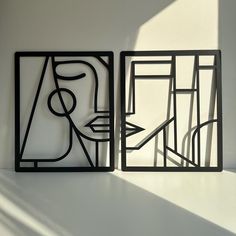 two black framed artwork pieces sitting on top of a white table next to each other