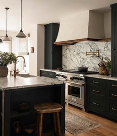 a kitchen with black cabinets and marble counter tops, an island in front of the stove