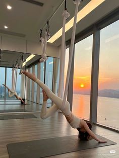 woman doing aerial yoga in front of large windows