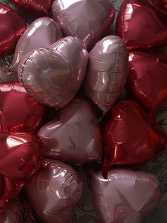 many heart shaped balloons are arranged in a pile on the floor and one is pink