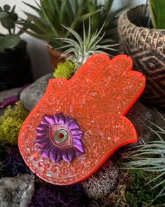 an orange brooch with a purple flower in it sitting on some rocks and succulents