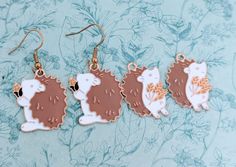 three hedgehogs are hanging from gold earwires on a blue floral background