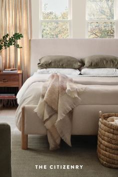 a bed with two pillows and blankets on top of it in front of three windows