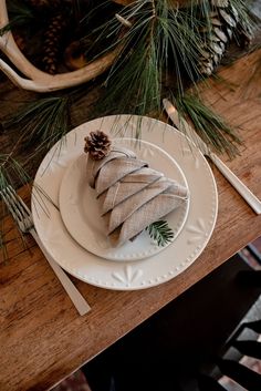 a white plate topped with a piece of cake next to a pine cone on top of a wooden table