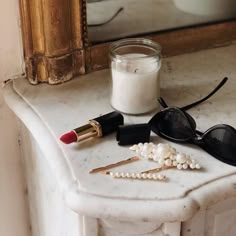 some lipstick, sunglasses and pearls on a marble table with a mirror in the background