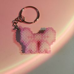 a pink and white beaded bow keychain on a pink surface with light coming from behind it