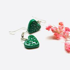 two green heart shaped earrings sitting next to pink flowers