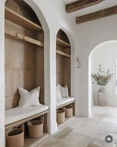 an arched entryway with benches and baskets on the floor, along with two vases filled with flowers