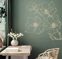 a room with green walls and white flowers on the wall next to a chair in front of a table