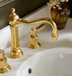 a gold faucet sitting on top of a white sink next to a vase with flowers