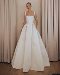 a woman standing in front of curtains wearing a white wedding dress with pockets on the skirt