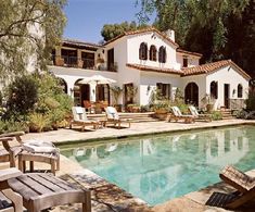 a house with a pool in front of it and lawn chairs around the pool area