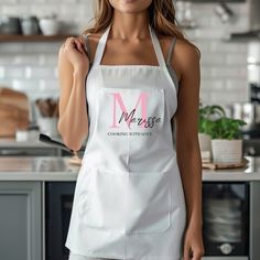 a woman wearing an apron and smiling at the camera while standing in front of a kitchen counter