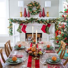 a dining room table set for christmas with candles and decorations on the fireplace mantel