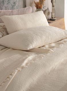 an unmade bed with white linens and decorative items on the nightstand next to it