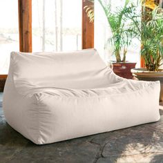 a white bean bag sitting on top of a stone floor next to potted plants