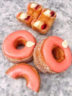 four doughnuts with pink icing and cream filling on top of a marble surface