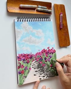 a person is drawing flowers on a notebook with colored pencils and watercolor paper