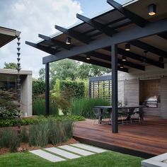 an outdoor patio with wooden decking and black pergolated roof, surrounded by green grass