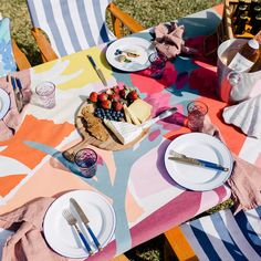 an outdoor table set with plates, silverware and fruit on it for a picnic