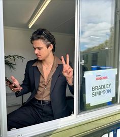 a man in a suit sitting on a window sill and making the peace sign