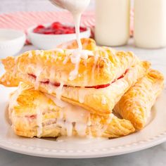 strawberry turnovers with cream being drizzled over them on a white plate