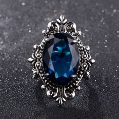 This gorgeous sterling silver ring is perfect for a person with a flare for vintage jewelry. The Blue Sapphire Peacock Vintage Ring features an oval blue sapphire as its centerpiece, encircled by small round white diamonds that catch the light gloriously and radiate life! From cornflower blue to velvety blue, there are multifarious shades of blue sapphire that gives it a silky tint. Characterized by the power of Shani or Saturn, Blue Sapphire displays violet to indigo and pale blue as well as da Sapphire Silver Ring, September Birthstone Rings, Sapphire Rings, Blue Gems, Unisex Ring, Lovely Ring, Glass Rings, Blue Jewelry, Anniversary Party