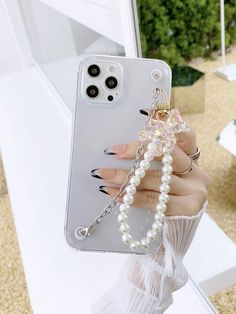 a woman holding up her phone case with pearls on the front and sides, while wearing a white dress