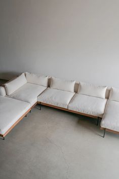 a white sectional couch sitting on top of a cement floor next to a wooden frame