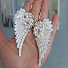 a hand holding two white angel wings with pearls and gold trimmings on them