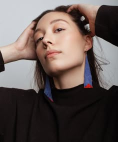 a woman with her hands on her head, wearing earrings and a black sweater is looking off to the side