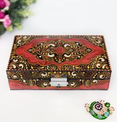 an ornate wooden box sitting on top of a white table next to a flower arrangement